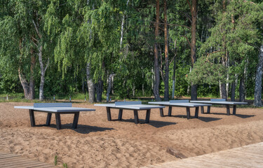 Tables for playing table tennis near the forest on the sand. River beach of Chaikovsky (Ural, Russia) in summer.