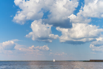 Small boat with a sail floats along the river against a blue sky with large voluminous clouds. Kama River (Ural, Russia).