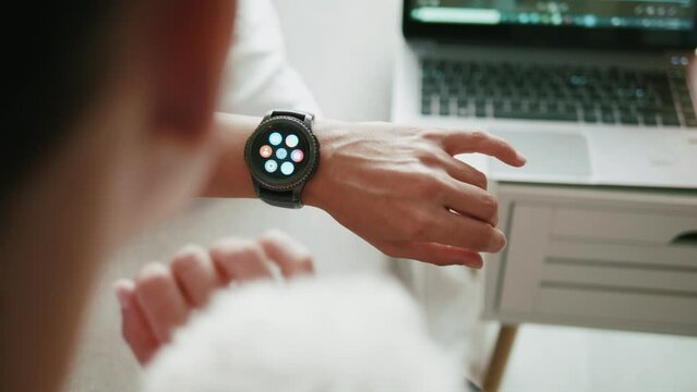 Mature woman sitting on the bed uses a smartwatch to check results after practicing outdoors.