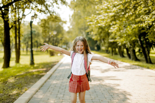 A cute schoolgirl with a backpack runs through the park and laughs. Elementary school, back to school, school time, school age