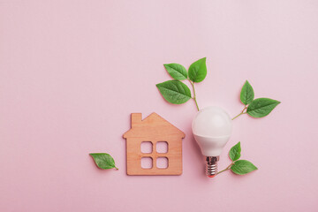Energy saving lightbulb with green leaves and wooden house symbol background. Save energy, eco home concept. Flat lay, top view