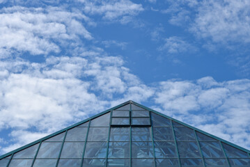 Abstract view of a modern buildings pointed roof leading to a blue sky with fluffy clouds. - Powered by Adobe