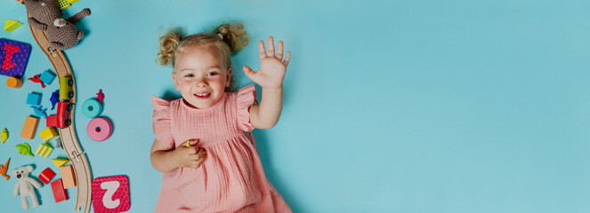 Happy little girl lying in the frame of plenty of toys