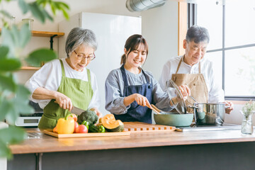 キッチンで料理する高齢者夫婦と若い日本人女性（料理教室）

