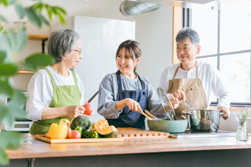 キッチンで料理する高齢者夫婦と若い日本人女性（家事代行・介護・）
