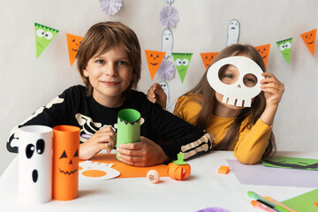 A little girl in a skeleton mask and a boy in a skeleton costume make zombie crafts for the...