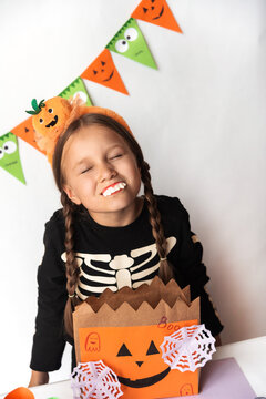 A little girl in a skeleton costume with a headband with a pumpkin and vampire teeth. Schoolgirl with a bag of sweets