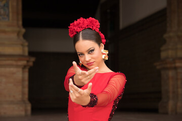 Portrait of young teenage woman in red dance suit with ruffles and red carnations in her hair doing...