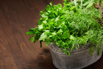 a top of bunch of green dill, parsley, salad and other greens in an iron bucket, dark wooden background, concept of fresh vegetables and healthy food