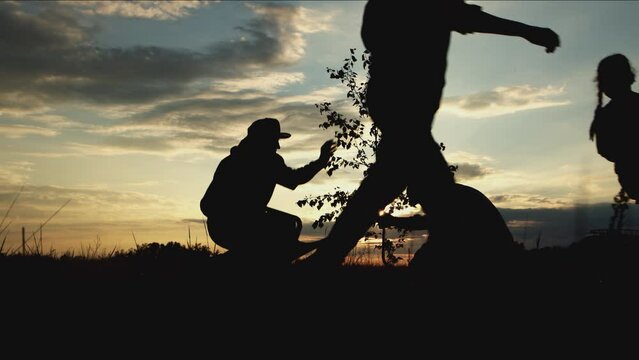 Silhouette of volunteers group of different human together watering, digging, planting tree in forest park at sunset outdoors. Team agricultural work, reforestation, environment care for save nature