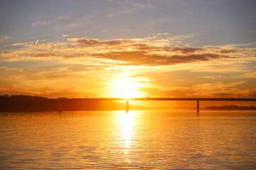 Obraz premium Beautiful bright orange sunset over the surface of the river and the bridge. Summer nature landscape