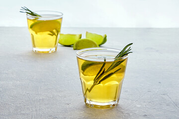 Two glass cup of homemade fermented kombucha tea with rosemary and lemon lime on a light gray concrete table
