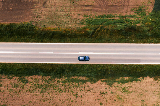 Aerial shot of passenger car driving along asphalt road through countryside landscape with no trees and shade on hot sunny summer afternoon