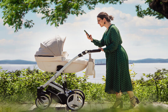 A young mother in a green dress walks with her baby. Mom takes a picture of a baby in a stroller while walking in the city