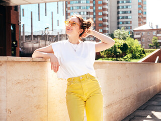 Young beautiful smiling hipster woman in trendy summer yellow jeans clothes. Carefree teen model posing in the street at sunset. Positive female outdoors. Cheerful and happy. In sunglasses