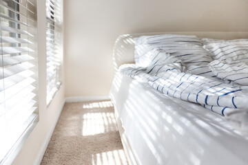 bright bedroom sunlited by morning sunbeams through the window blinds