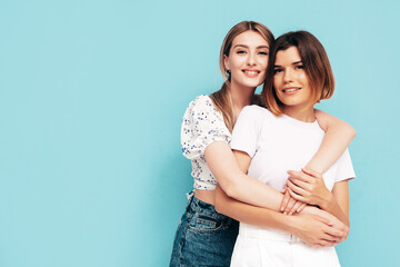 Two young beautiful smiling brunette hipster female in trendy summer shorts clothes. Sexy carefree women posing near blue wall. Positive models having fun. Cheerful and happy. Hugging