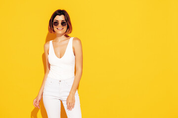 Obraz premium Young beautiful smiling female in trendy summer white jeans clothes. Carefree woman posing near yellow wall in studio. Sexy positive model having fun indoors. Cheerful and happy
