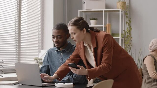 Medium slowmo of young Caucasian woman showing working program on laptop to new employee on his first day in office