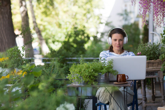 work from vacation home, remote workers. middle aged woman in headphones using a laptop, connecting to the Internet  in the garden near the house. Working from Anywhere.