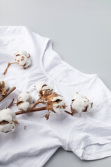 Fototapeta na wymiar White cotton t-shirt and a branch of cotton on a gray background