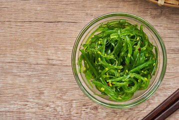 top view or flat lay wakame seaweed salad with sesame seed in glasses bowl and wooden chopstick on wood table background          