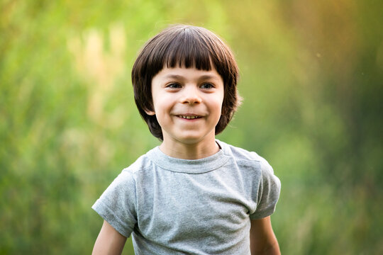 Portrait of little adorable boy against green trees outdoors in summer