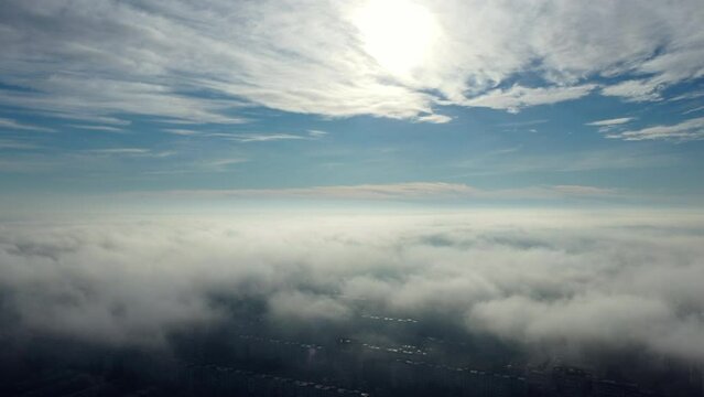 Aerial drone view flight over clouds fog mist, buildings roof in city and under white clouds in blue sky on sunny day. Abstract natural urban background. Atmosphere. Top view fog cloudy and rooftops