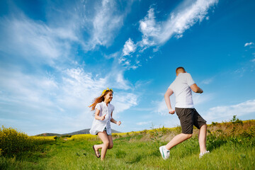 Teenagers: brother and sister are running and enjoying weather, in meadow against cloudy sky