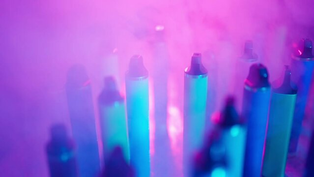 Lots of E-Cigarettes and Vapes with Smoke in Neon Lighting. Concept of Bad Habits. Modern Smoking Electronic Cigarettes. Slow Motion