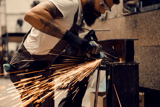Heavy industry worker using grinder and cutting metal parts at workshop.