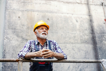 A senior heavy industry worker with a helmet on his head leaning on the railing at the facility and...