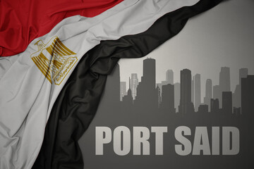 abstract silhouette of the city with text Port Said near waving colorful national flag of egypt on a gray background.