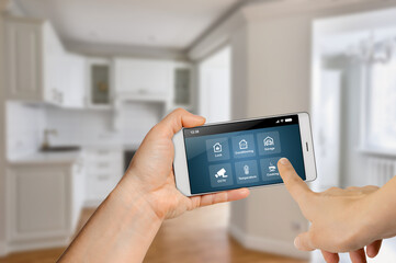 Woman hands holding mobile phone with smart home app against kitchen room background