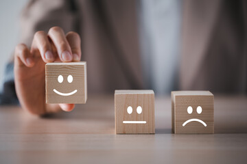 closeup businesswoman hand picking happy emotion face on wooden cube arranged on table for satisfaction survey