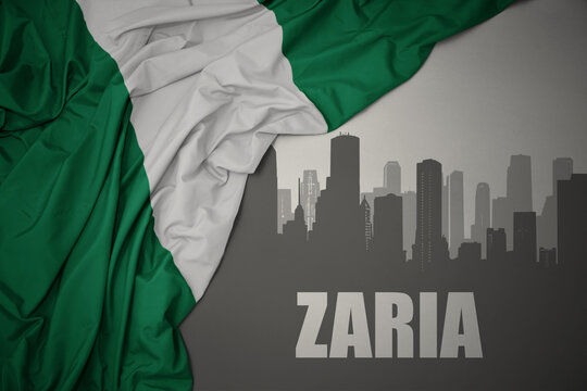abstract silhouette of the city with text Zaria near waving colorful national flag of nigeria on a gray background.