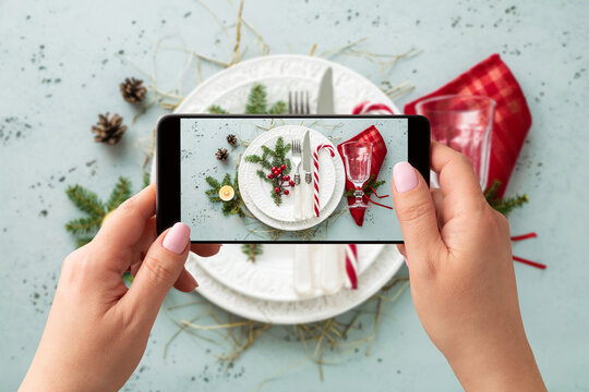 Woman taking photo of Christmas table setting with smartphone. Winter decorations for social media.