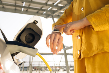 Businesswoman plugging in charging cable to to electric vehicle. Female hand inserts power...