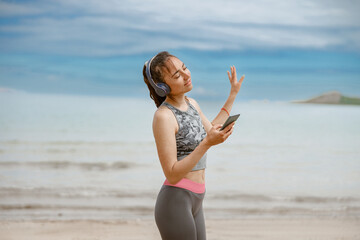 Fototapeta na wymiar Woman in sportswear listening music on headphones by the beach on background of ocean