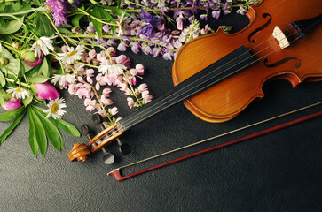 Violin, bow and a bouquet of wild flowers on a dark background.