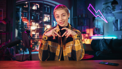 Attractive Young Female Talking Into Microphone While Recording Radio Show from Her Loft Apartment. Happy Woman with Short Hair Talking on Camera and Recording Podcast Live on Social Media.