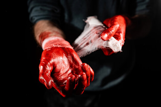 A man covered in blood bandages his hands.