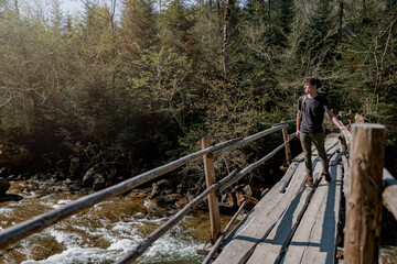 Fototapeta na wymiar Young man traveler standing on wooden bridge and looking at fast mountains river in forest.