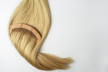 A strand of blonde hair with a wooden comb on it lying on a white background