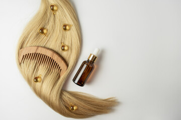 A natural essential oil or serum for hair care in golden capsules lying on a strand of  blonde hair. Hair care and smoothing concept