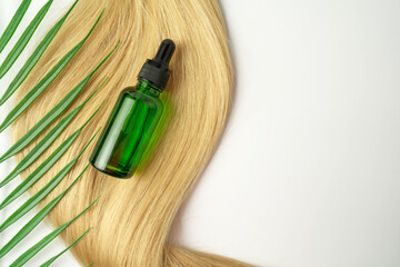 A  dropper bottle of green CBD oil or serum for hair care in golden capsules lying on a strand of  blonde hair. Hair care and smoothing concept