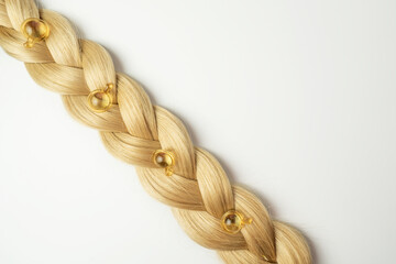 A natural essential oil or serum for hair care in golden capsules lying on a strand of  blonde...