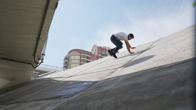 Male athlete jumps on a slope and slides down on a bright sunny day. Guy performs a parkour trick. Slow motion.