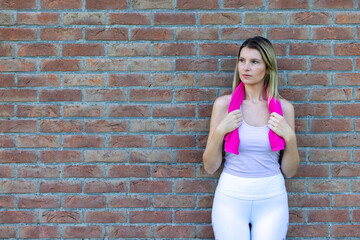 Portrait of an attractive sexy young Caucasian blonde sporty woman in sports clothing with towel around neck resting after a workout. High quality photo