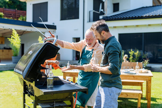 Senior father with adult son grilling outside on backyard in summer family during garden party